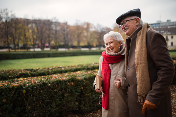 Happy senior friends on walk outdoors in a town park in autumn, holding and laughing.