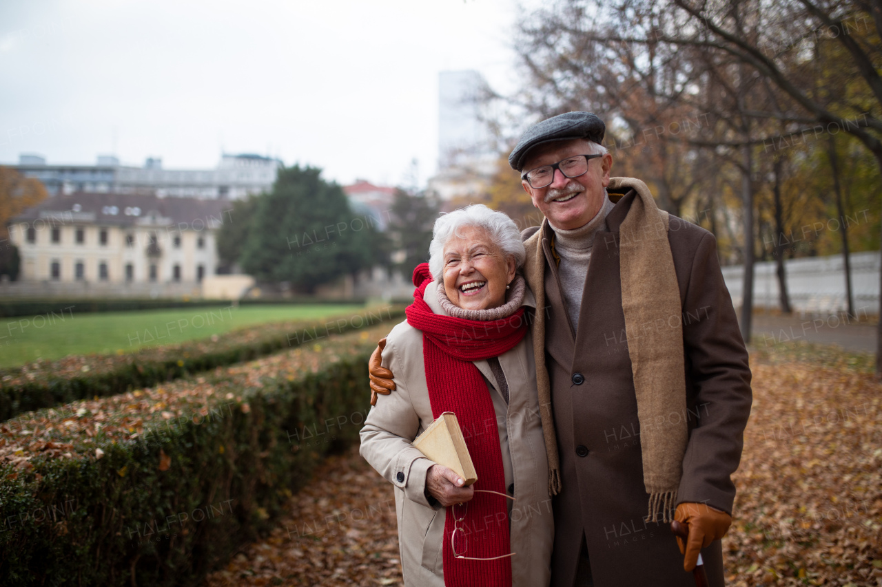 A happy senior couple on walk outdoors in park in autumn, embracing, laughing and looking at camera