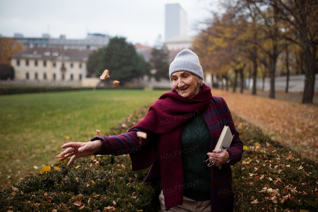 A happy senior woman with book on walk in town park in autumn.