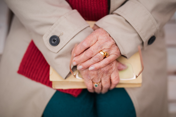 A close up of elegant senior woman holding book and sitting outdoors on bench.