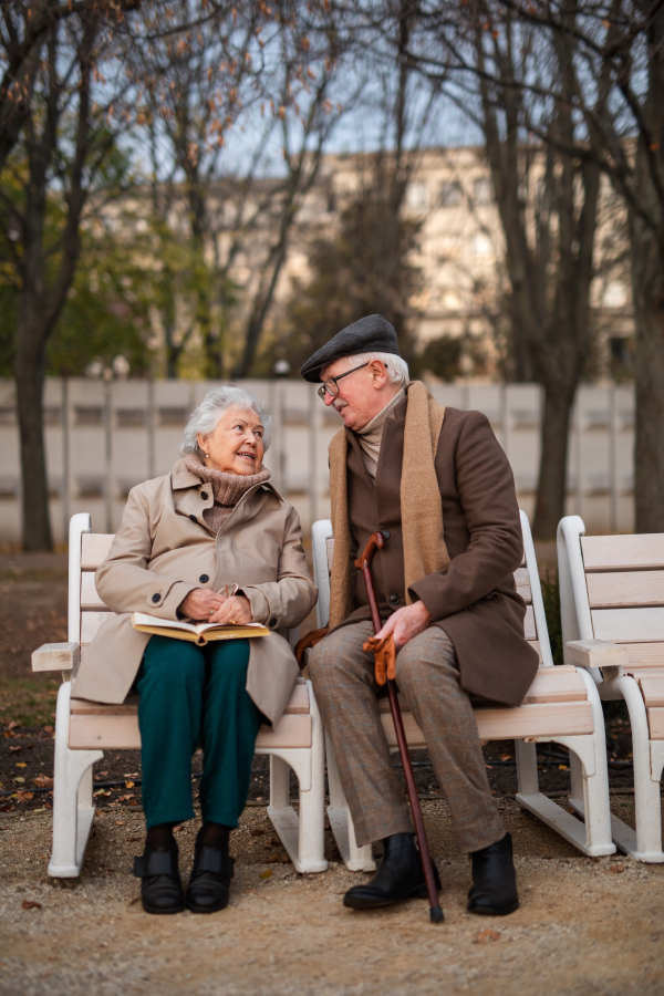 A happy senior friends on sitting on bench and talking outdoors in park on autumn day.