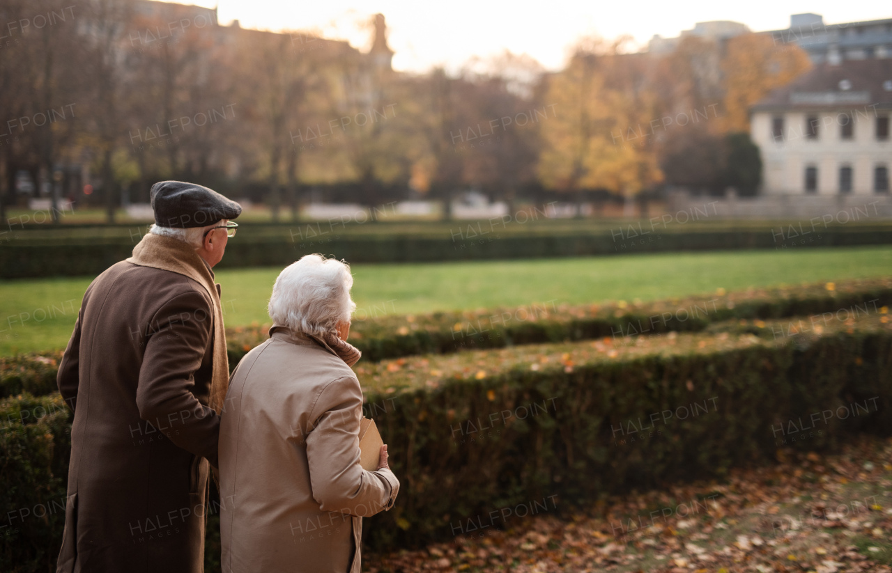 A happy senior couple on walk outdoors in town park in autumn.