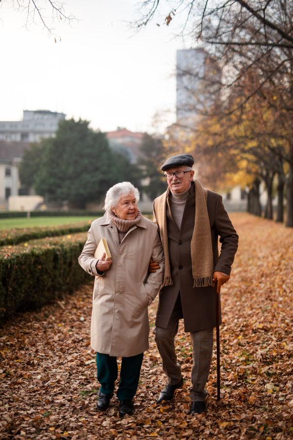 A happy senior couple on walk outdoors in town park in autumn.