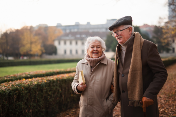 A happy senior friends on walk outdoors in town park in autumn, looking at camera.