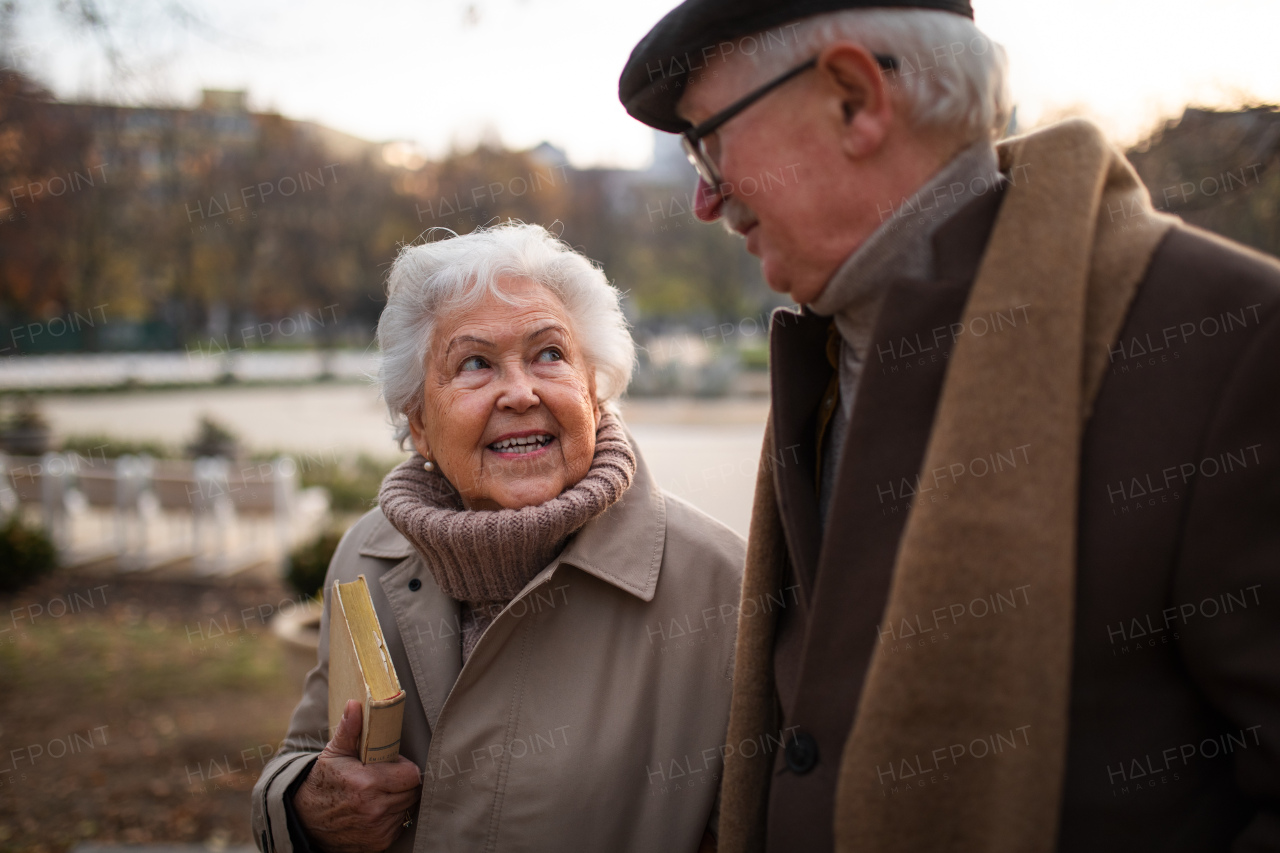 Happy senior friends on a walk outdoors in town park in autumn, talking.