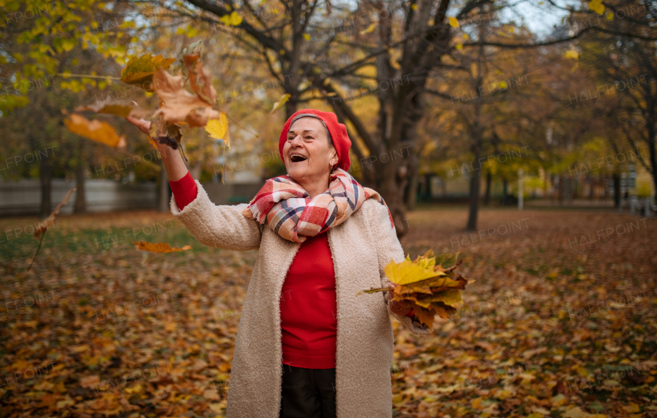 Happy senior woman throwing colorful leaves in the air, enjoying autumn days.