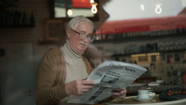 Elegant senior man with silver hair reading newspaper in a cafe.