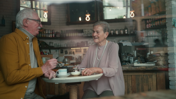 Happy senior couple sitting indoors in a cafe drinking coffee, talking and having nice time together.