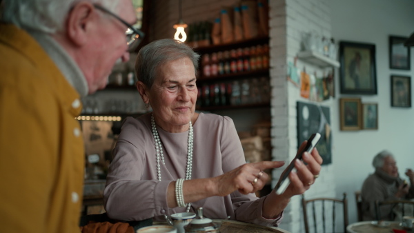 Senior woman showing photos in her mobile phone to her friend in a cafe.