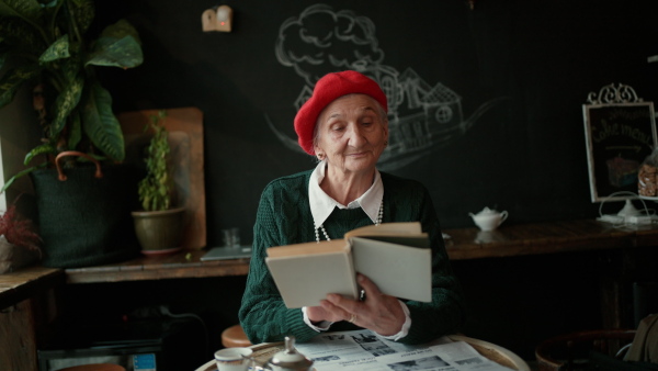 Elegant senior woman with silver hair and white pearls reading book in cafe.