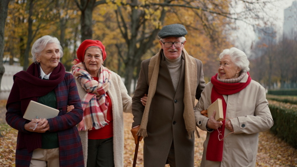 A happy senior friends on walk outdoors in town park in autumn, looking at camera.