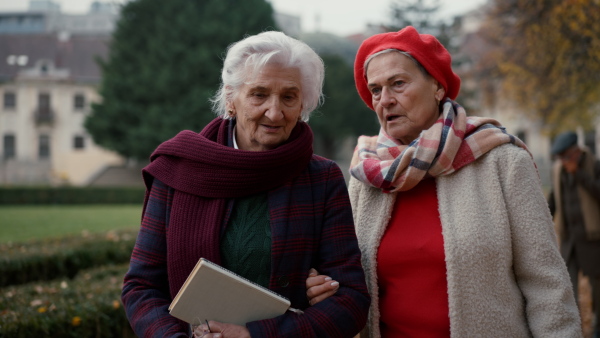 Happy senior women friends on a walk outdoors in town park in autumn.