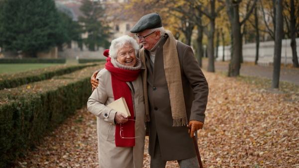 A happy senior friends on walk outdoors in town park in autumn, looking at camera.