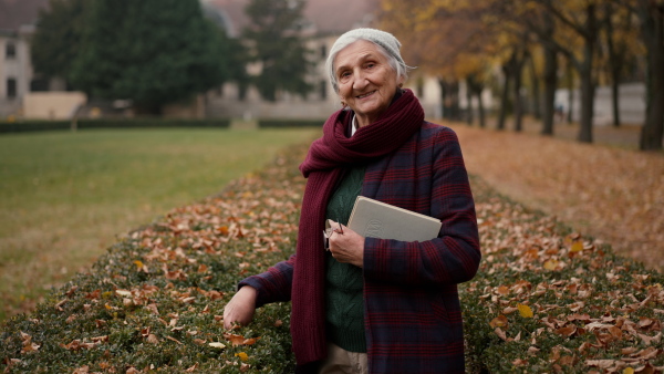 A happy senior woman with book on walk in town park in autumn.