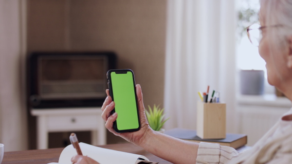 A senior woman having a call on smartphone with green screen. Lockdown concept.