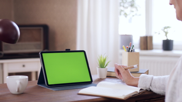 A senior woman having a call on tablet with green screen. Lockdown concept.