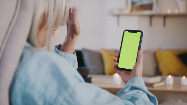 Senior woman having an online consultation on smartphone with green screen. Lockdown concept.