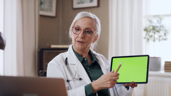 A senior woman doing an online presentation on tablet with green screen. Lockdown concept.