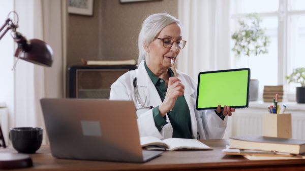 A senior woman doing an online presentation on tablet with green screen. Lockdown concept.