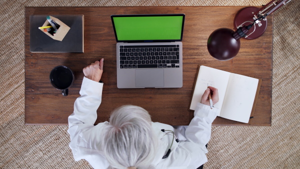 A top view of senior doctor having an online consultation on laptop with green screen. Lockdown concept.