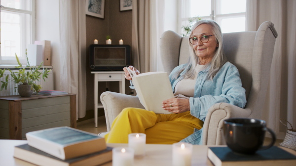 Beautiful senior woman relaxing with book at home, looking at camera.