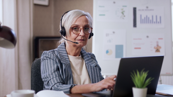 A senior woman working from home office, looking at camera. Lockdown concept.