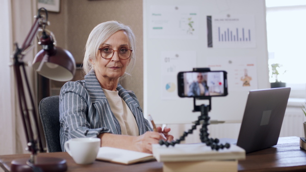 A senior woman streaming an online presentation, looking at camera. Lockdown concept.