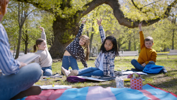 A teacher with small children sitting outdoors in city park, learning group education concept.