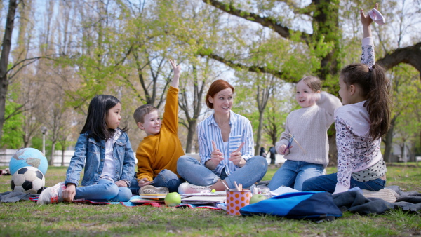 A teacher with small children sitting outdoors in city park, learning group education concept.