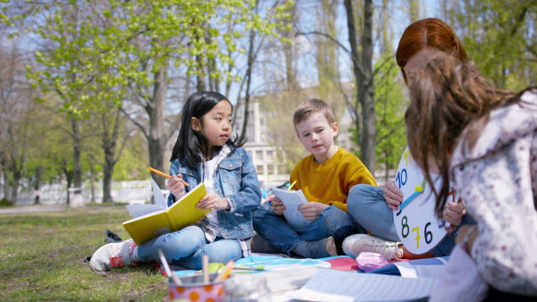 A teacher with small children sitting outdoors in city park, learning group education concept.