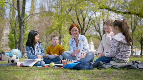 A teacher with small children sitting outdoors in city park, learning group education concept.