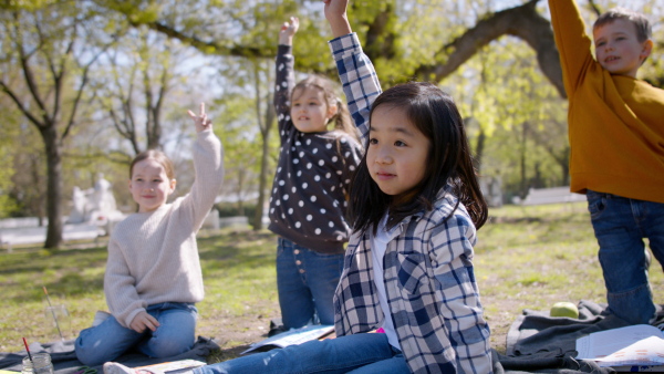 A small children sitting outdoors in city park, learning group education concept.