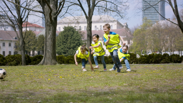 Happy small children playing football outdoors in city park, learning group education concept.