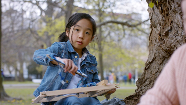 Small japanese girl with hand loom sitting outdoors in city park, looking at camera. Learning group education concept.