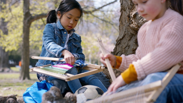 Small japanese girl with hand loom sitting outdoors in city park. Learning group education concept.