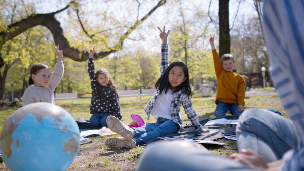 A teacher with small children sitting outdoors in city park, learning group education concept.