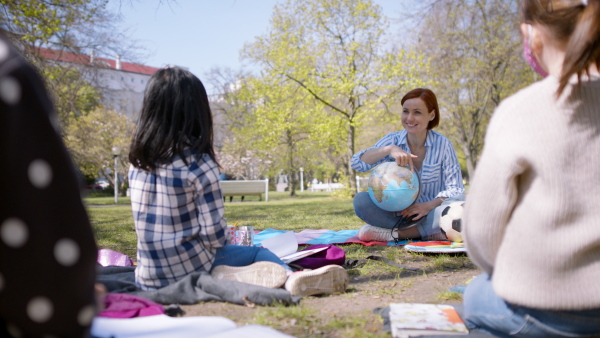 A teacher with small children sitting outdoors in city park, learning group education concept.