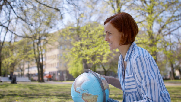 A teacher with globe sitting outdoors in city park, learning group education concept.