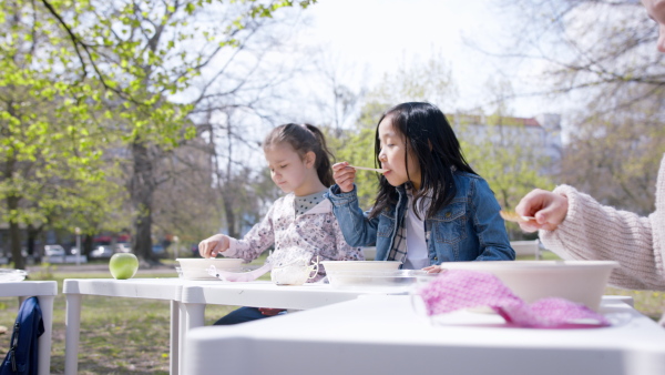 Happy small children eating lunch outdoors in city park, learning group education concept.