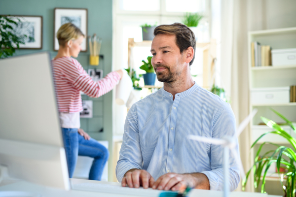 A mature businessman with computer and partner working indoors in home office.