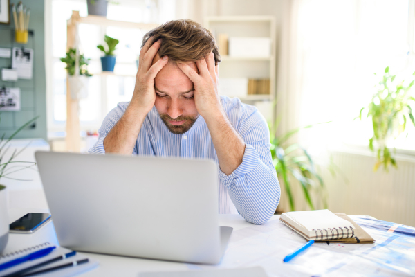 Frustrated and disappointed mature businessman with laptop indoors in home office, working.