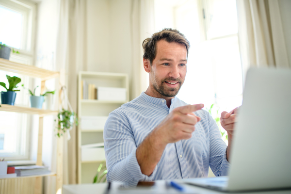 Mature businessman having video call on laptop at home, gesturing.