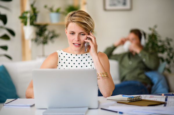 Cheerful young businesswoman with laptop and telephone indoors in home office, working.