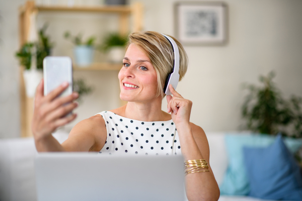 Cheerful young businesswoman indoors in home office, taking selfie when working.