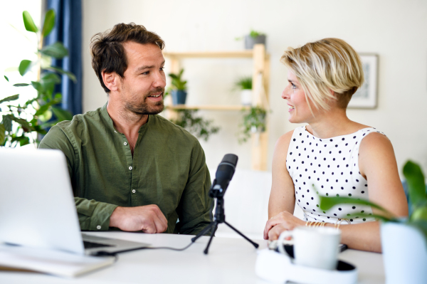 Front view of happy couple with microphone having video call on laptop indoors at home.