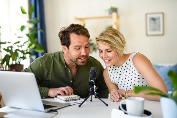 Front view of happy couple with microphone having video call on laptop indoors at home.