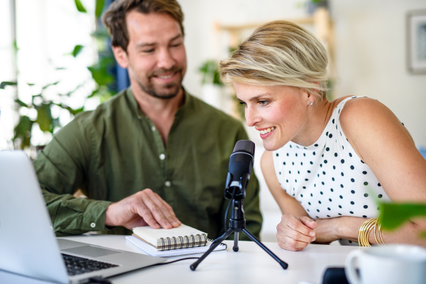 Front view of happy couple with microphone having video call on laptop indoors at home.