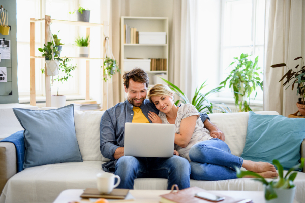 Front view of happy couple in love sitting indoors at home, using laptop.