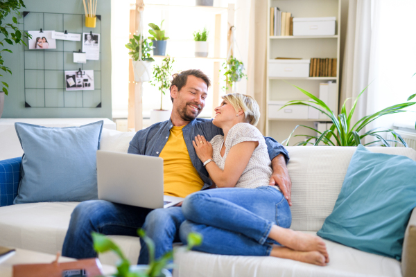 Front view of happy couple in love sitting indoors at home, using laptop.