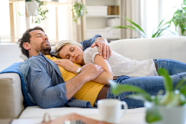 Happy couple in love lying on sofa indoors at home, sleeping.